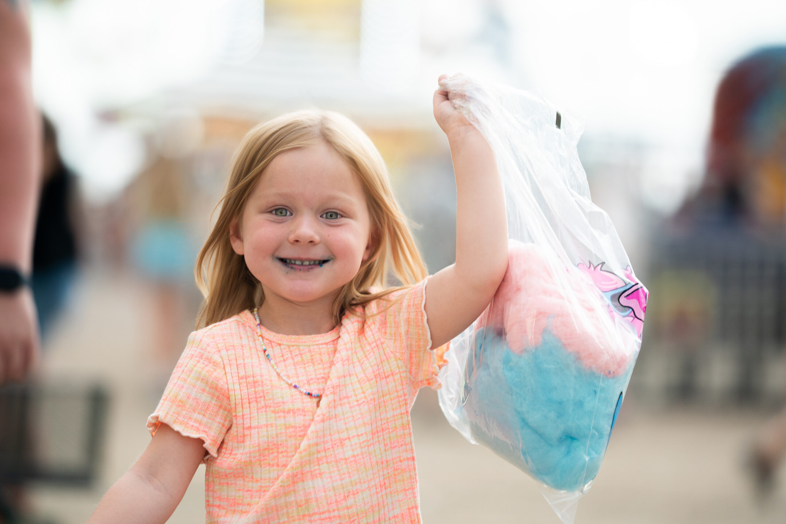 Child smiling and holding pink and blue cotton candy at the county fair