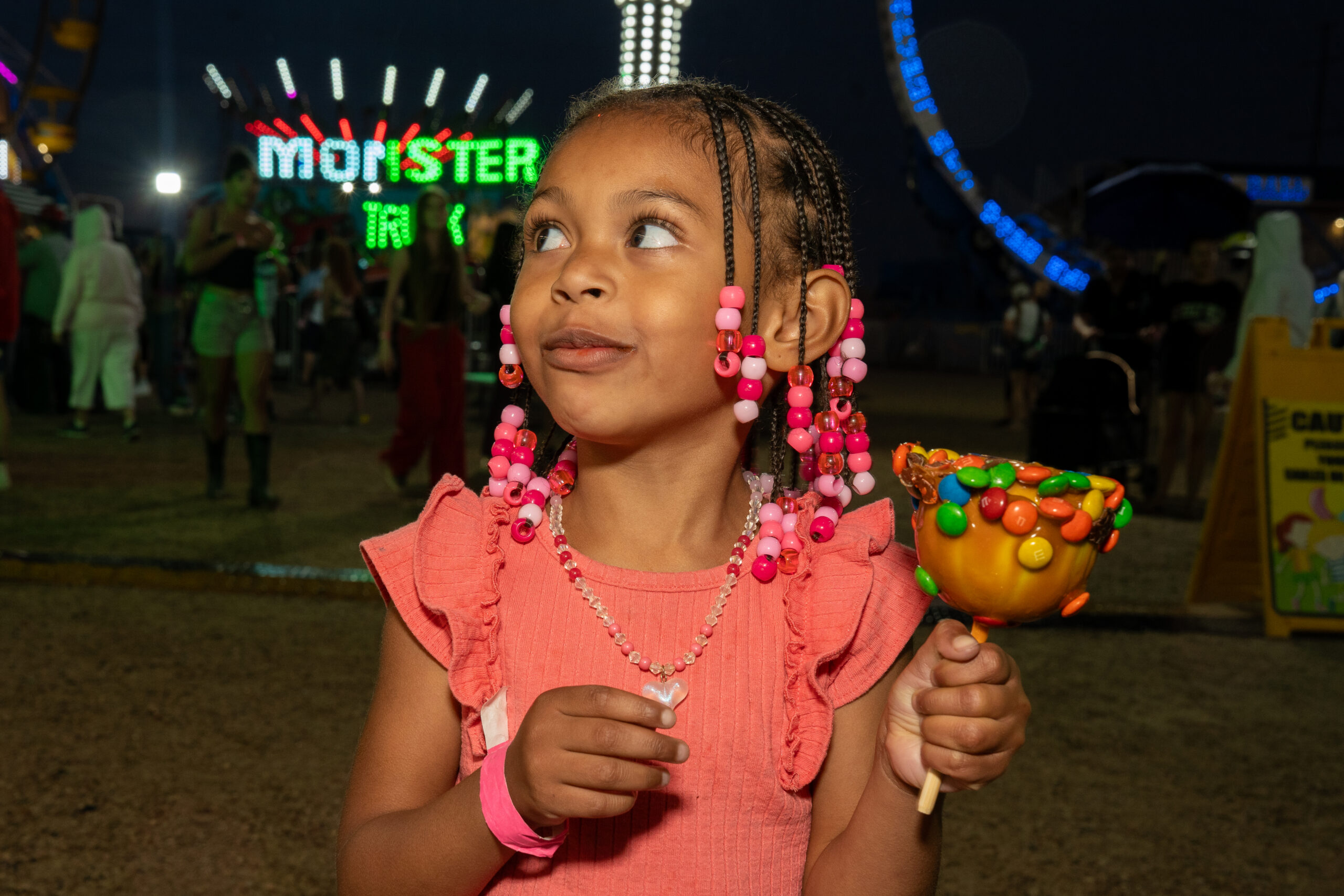 Child holding a candy-coated apple beneath carnival lights